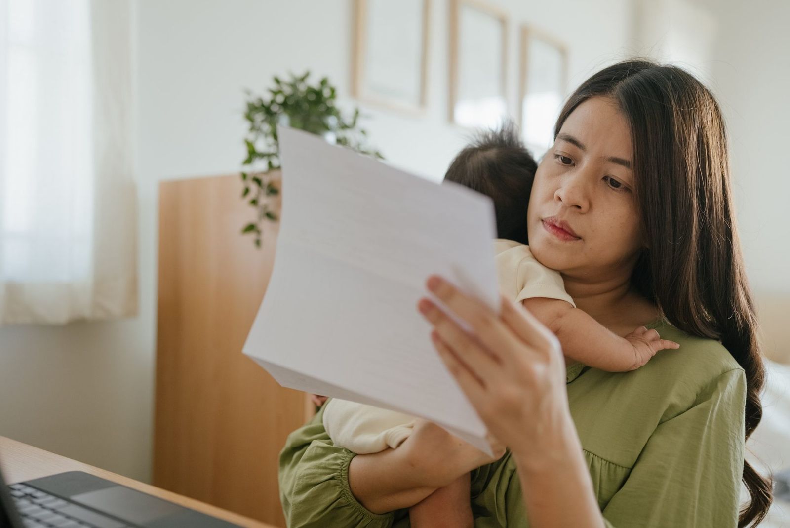 Working mother holding her baby while reviewing bills at home